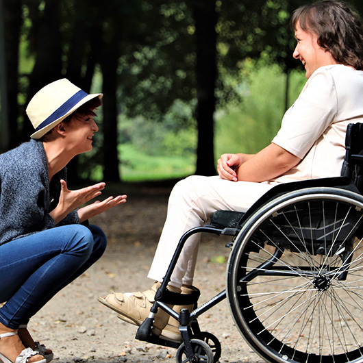 Gut gelaunte Frau unterhält sich mit lachender Rollstuhlfahrerin