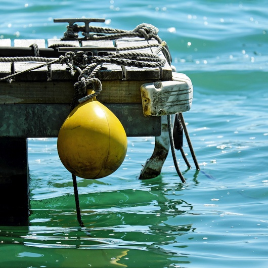 Eine gelbe Boje hängt an einem Steg über dem Wasser. Bild von Ilona Frey auf Pixabay.