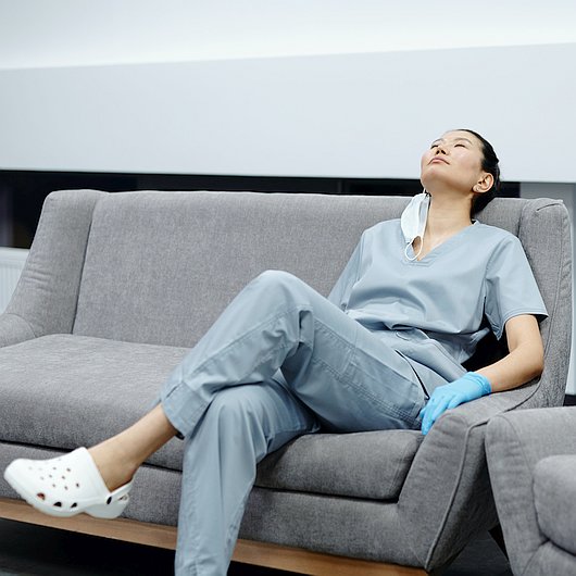 Eine Pflegerin sitzt erschöpft auf einem Sofa.