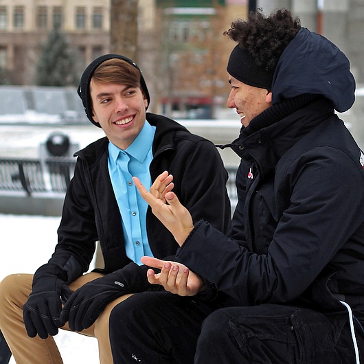Zwei junge Männer sitzen auf einer Bank und unterhalten sich.