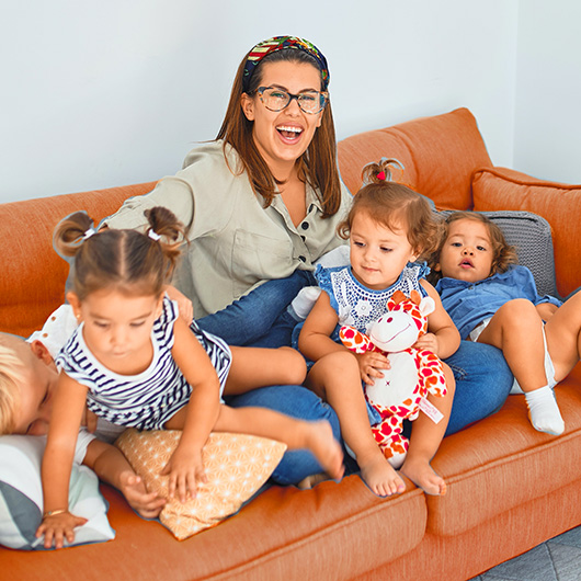 Lachende Mutter mit vier kleinen Kindern auf einem Sofa