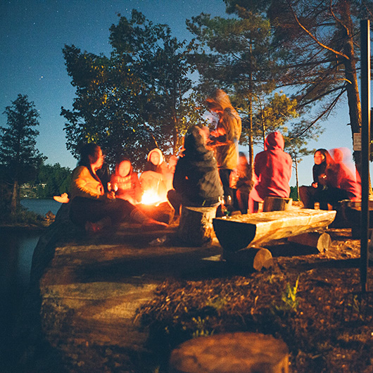 Jugendgruppe sitzt nachts am offenen Feuer in der freien Natur