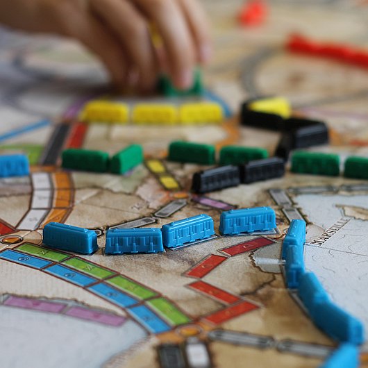 Eine Hand bewegt eine Spielfigur auf einem Brettspiel