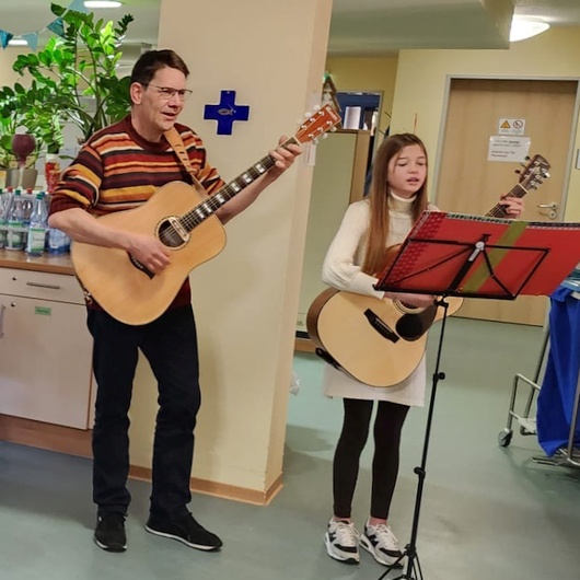 Ein Mann und ein Mädchen begleiten die Gesangsgruppe Hessfeld mit der Gitarre beim Adventssingen im Seniorenzentrum Drei Eichen.
