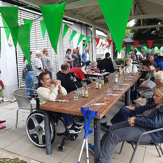 Ein Sommerlich geschmücktes Pavillon, und viele Tische an denen Menschen sitzen und lächeln