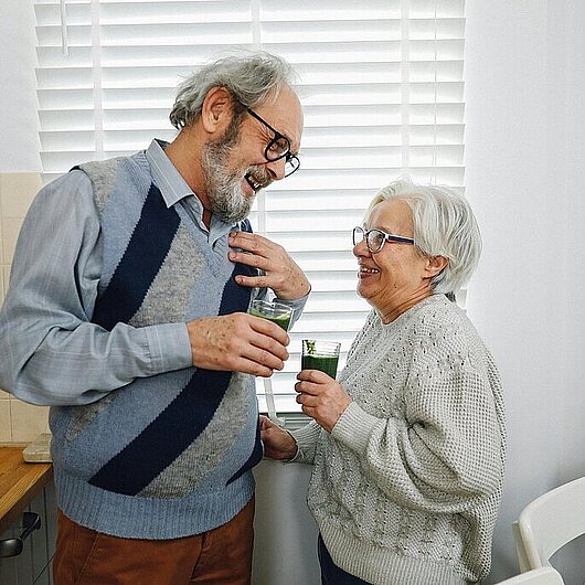 2 Senioren stehen in der Küche, trinken etwas und unterhalten sich