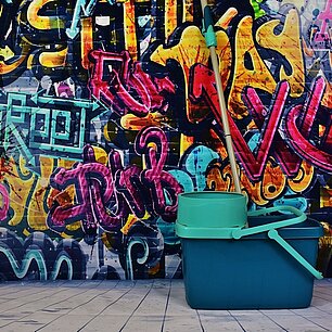 Ein Putzeimer vor einer Graffitiwand (Bild von Alexa auf Pixabay)