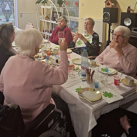 Senioren sitzen am Tisch und prosten sich zu.