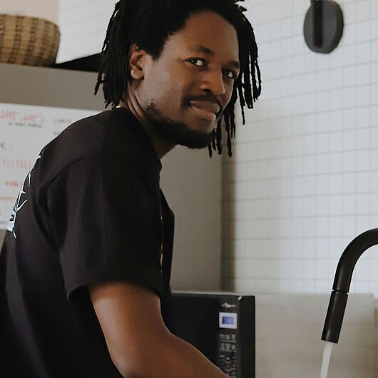 Ein junger Mann am Spülbecken in einer Küche (Foto: Good Faces // unsplash)