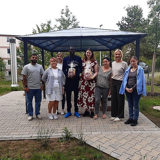 Ein Gruppenbild von 8 Menschen, in der Mitte stehen die beiden Schüler mit Geschenk.