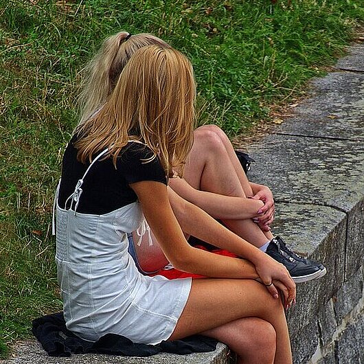 Zwei Mädchen sitzen auf einem Mäuerchen und unthalten sich (Foto: Wolfgang Eckert  // pixabay)