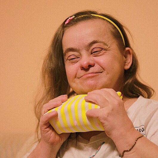 Frau mit Down-Syndrom, die fröhlich einen Geschenkesack umarmt und Glück ausstrahlt. (Foto: Daria // pexels)