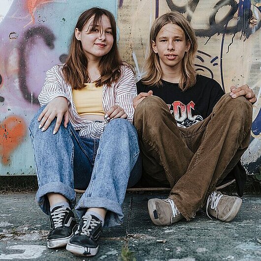 Zwei Jugendliche sitzen entspannt an einer Mauer mit Graffiti (Foto: Olia Danilevich // pexels)