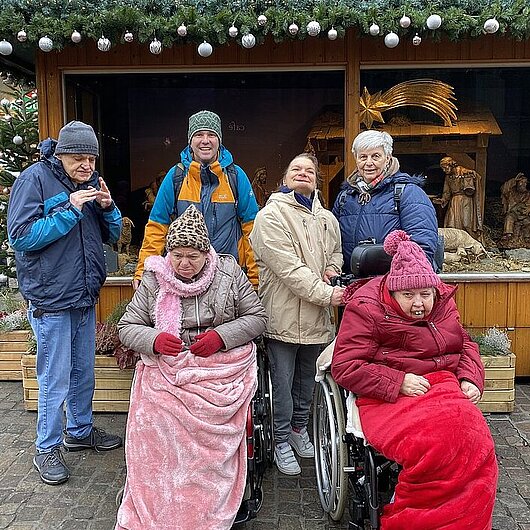 Bewohner:innen der Berner Straße mit Heilerziehungspfleger vor einem Weihnachtsstand
