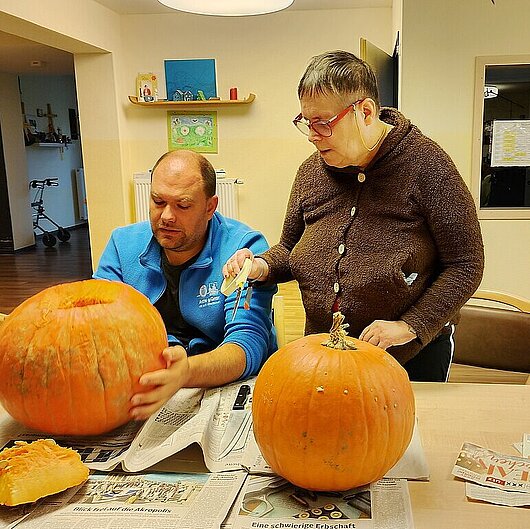 Man sieht zwei Personen beim Kürbis schnitzen